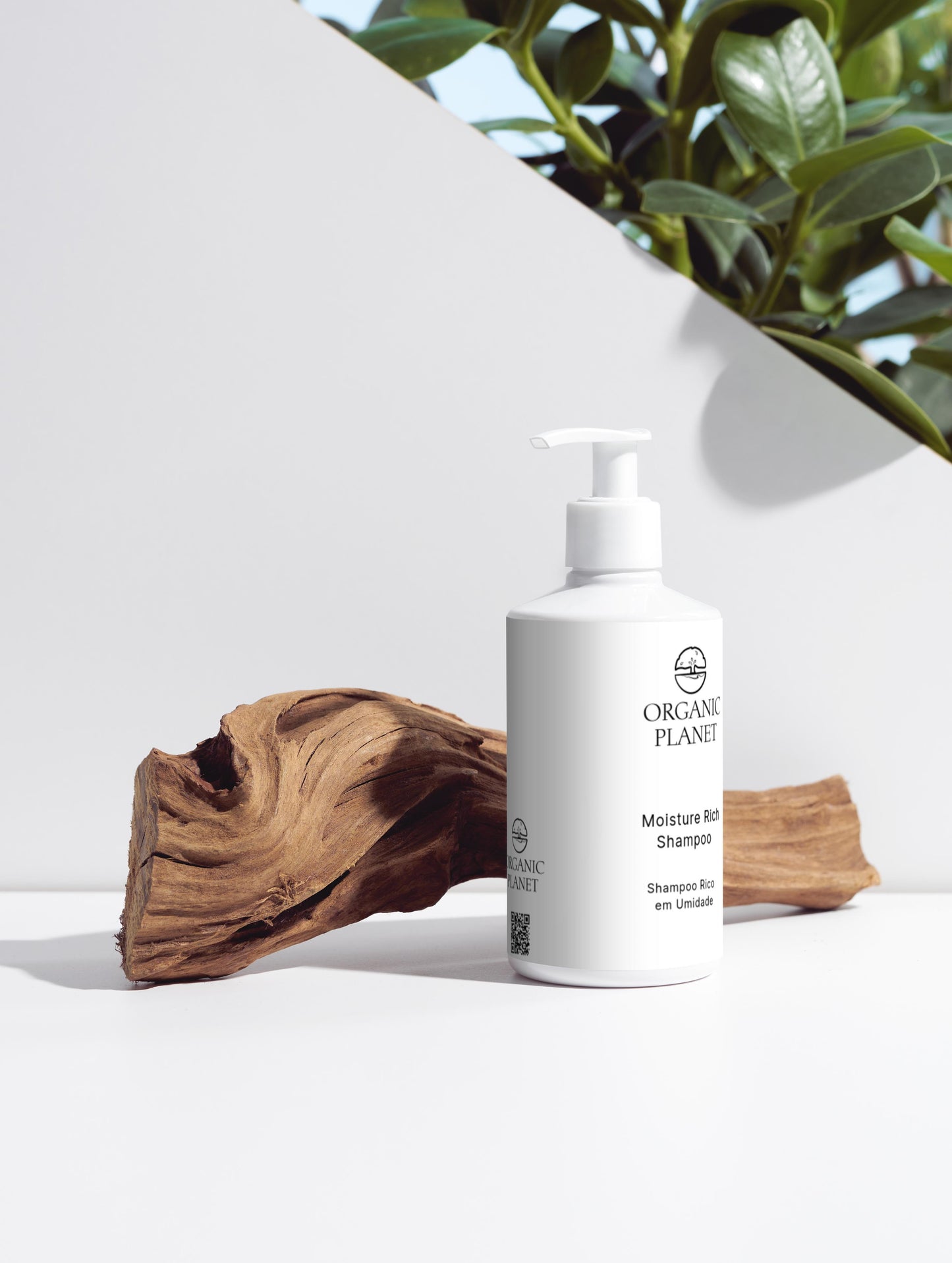 White bottle of Organic Planet shampoo on a white surface with a piece of wood and greenery in the background.